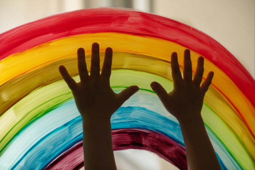 Child's hands touch painting rainbow on the window