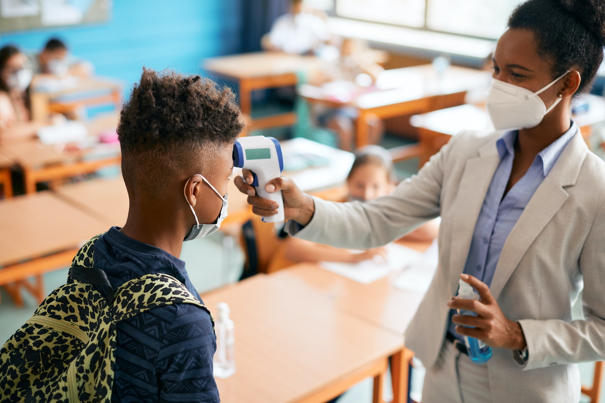 Elementary school teacher measuring temperature of schoolboy in classroom due to coronavirus.