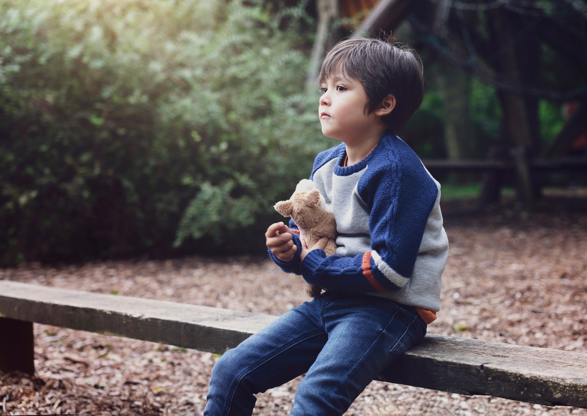 Lonely kid hugging dog toy sitting alone in the playground,Sad child boy sitting with his toy