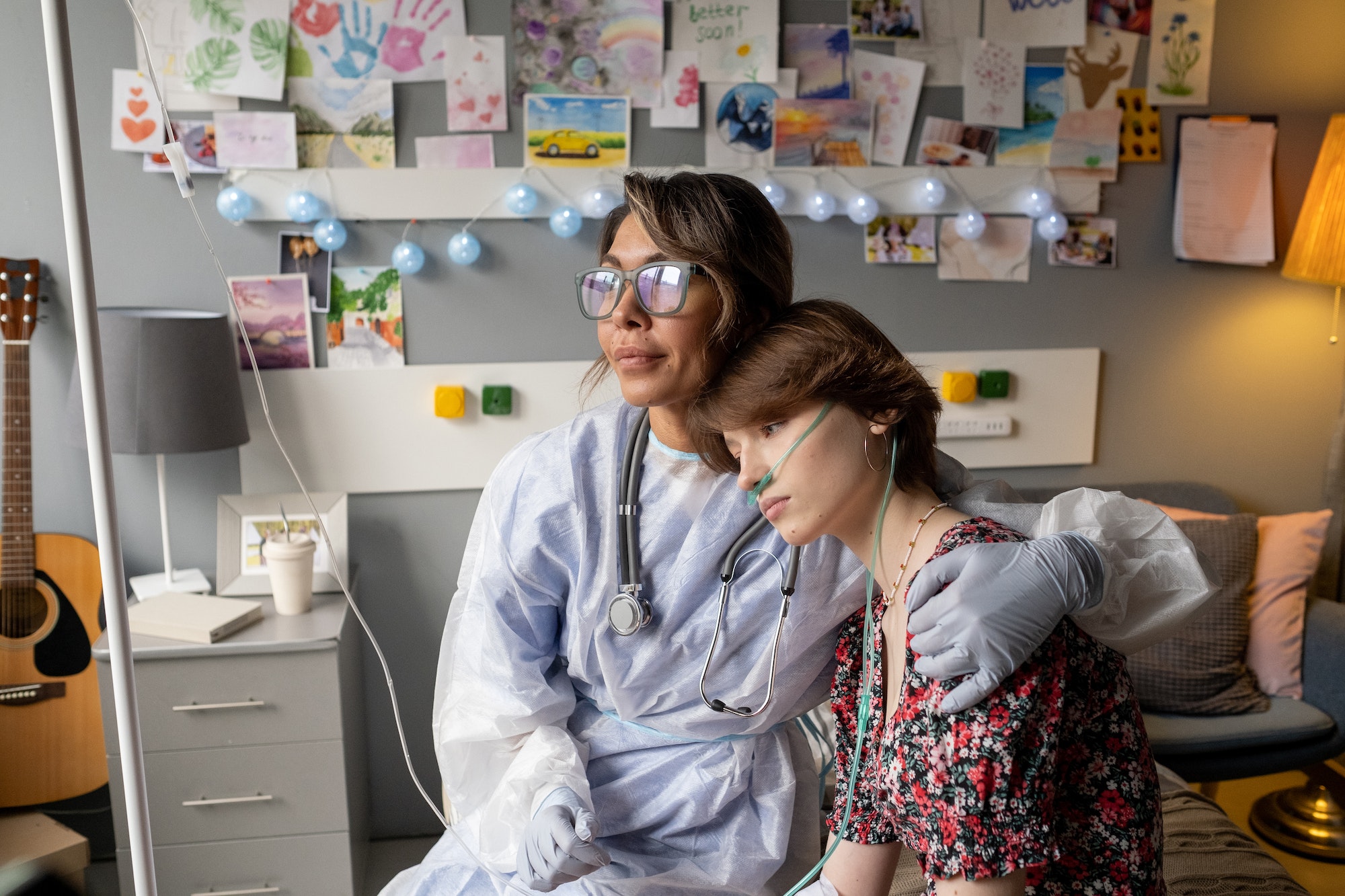 Nurse in workwear and eyeglasses embracing teenage patient