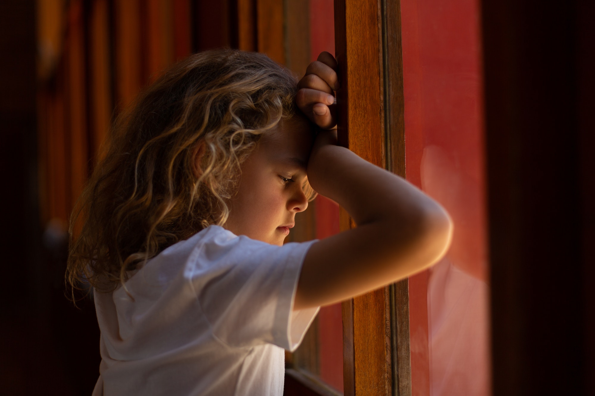 Sad schoolgirl leaning with her head on her hands against a window at school