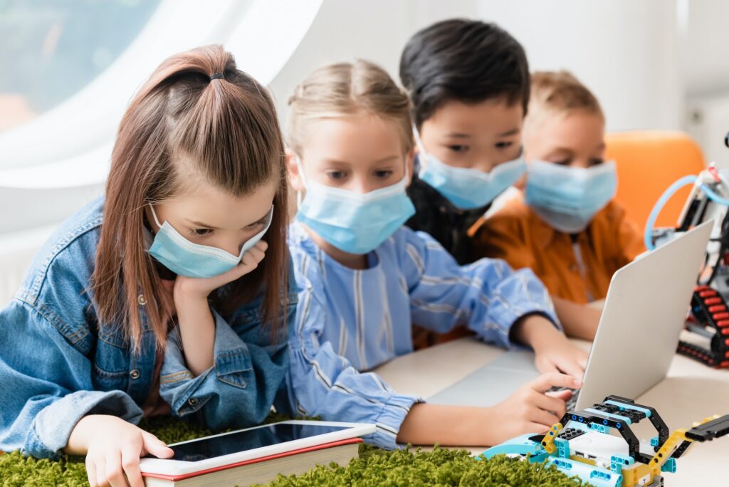Selective focus of multiethnic schoolkids in medical masks using gadgets while programming robot in
