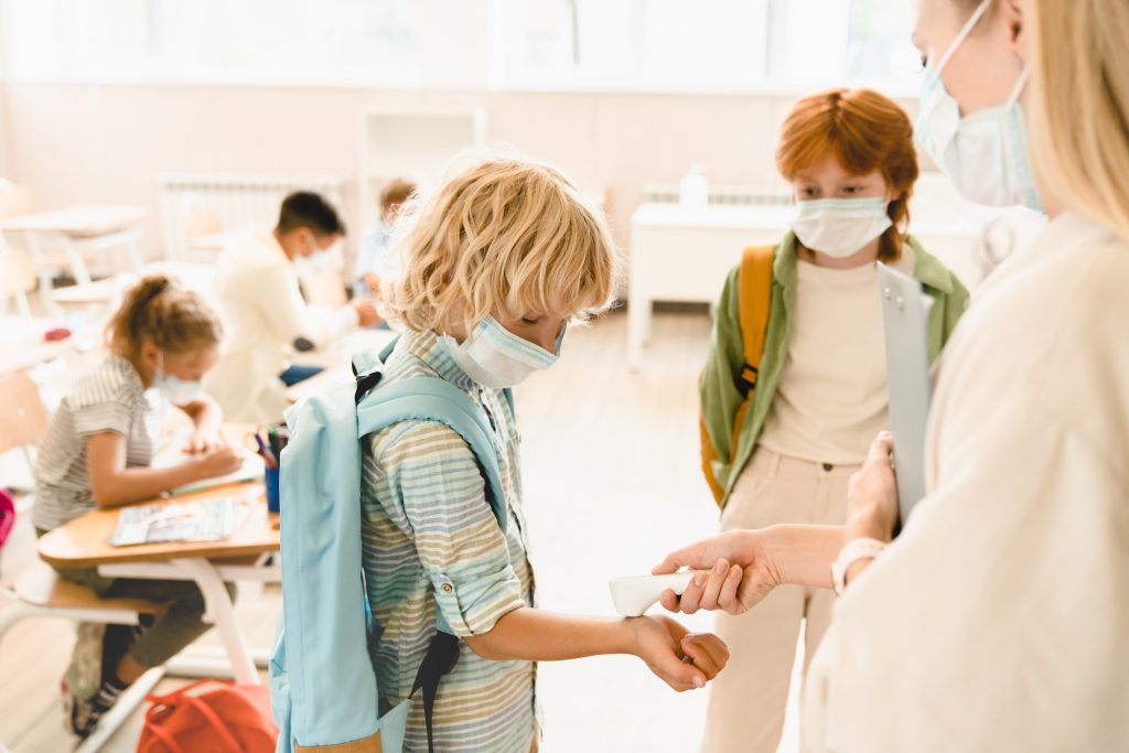 Teacher measuring temperature her students classmates schoolchildren before lesson