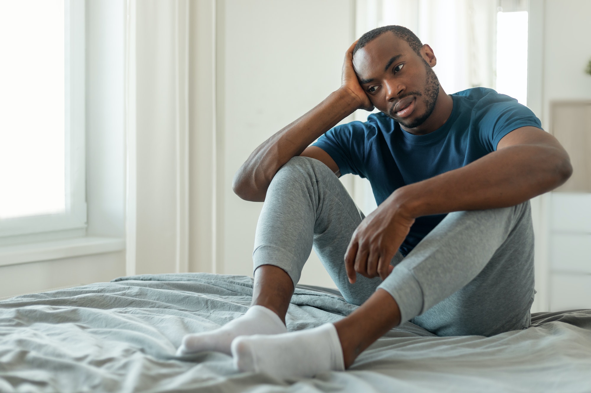 Unhappy Black Male Thinking About Loneliness Sitting In Modern Bedroom