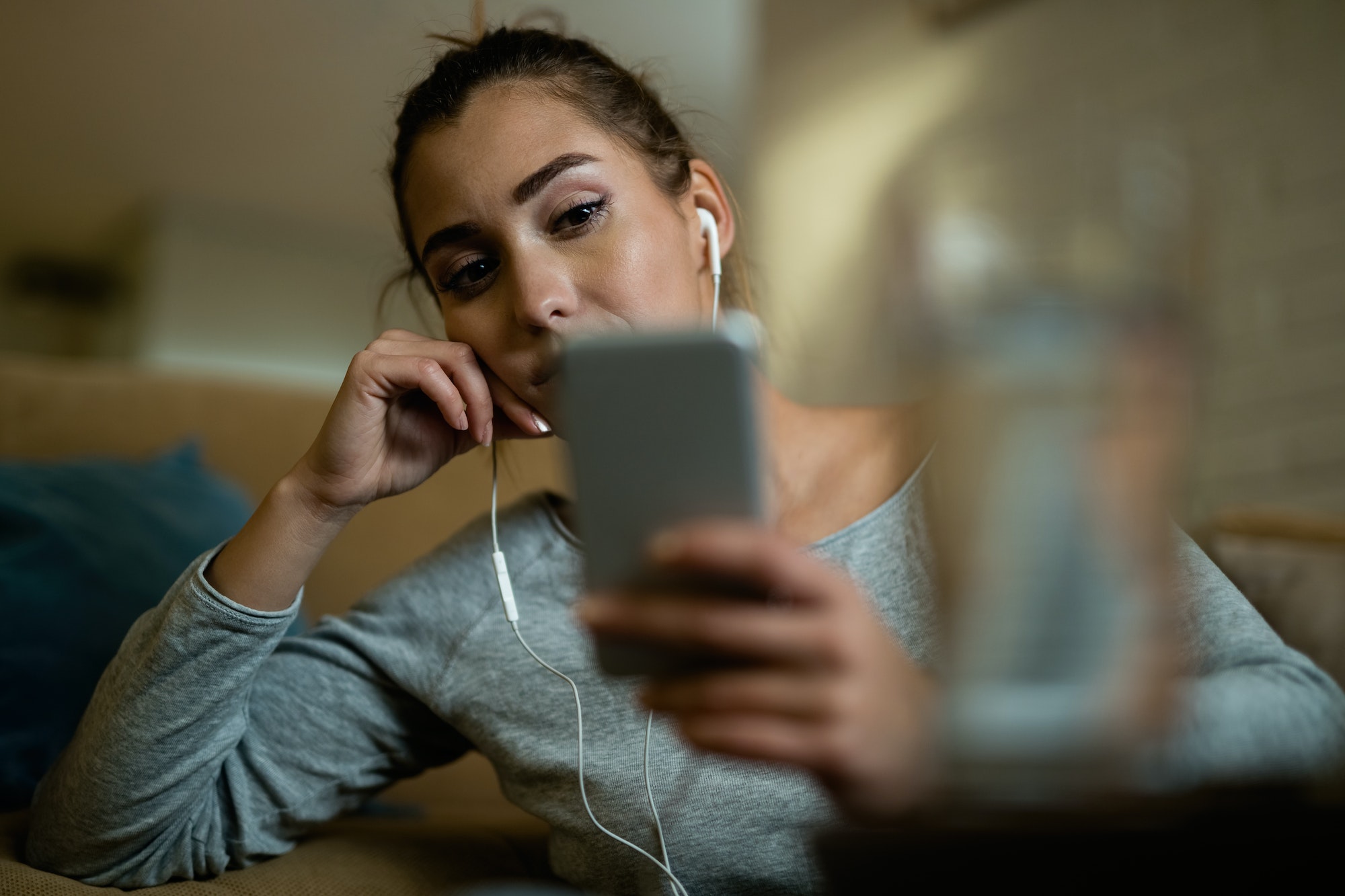 Young sad woman text messaging on mobile phone at home.