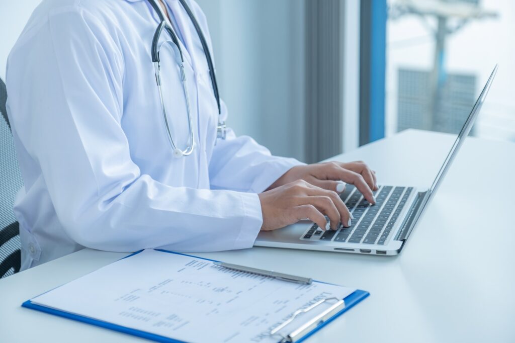 The doctor hand texting to the laptop and records the health examination results and medication